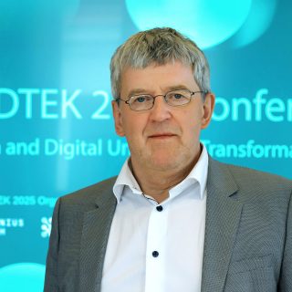 Man with grey hair and suit against a blue backgrond with light text