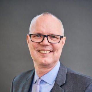 Portrait of a smiling man in a suit against a grey background.