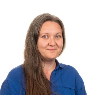 Portrait of a smiling woman with long hair wearing a blue shirt against a white background.